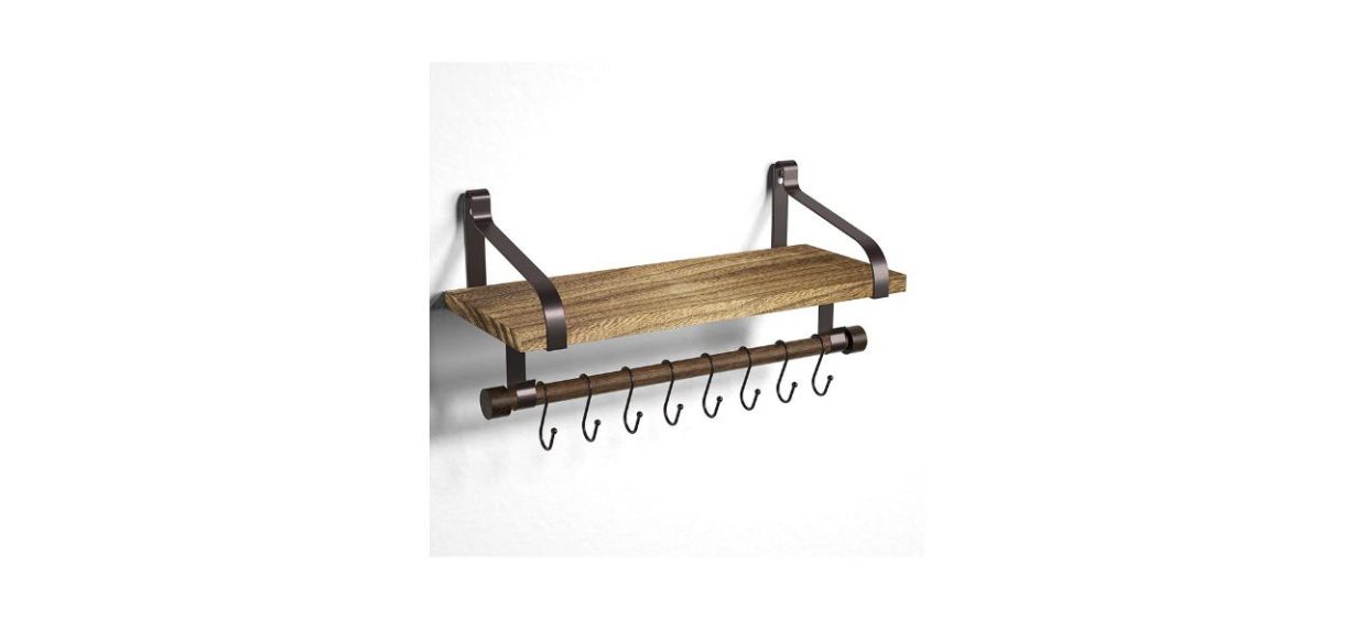 A wooden floating shelf mounted on a wall that has 8 hooks on the bottom of it to hang things
