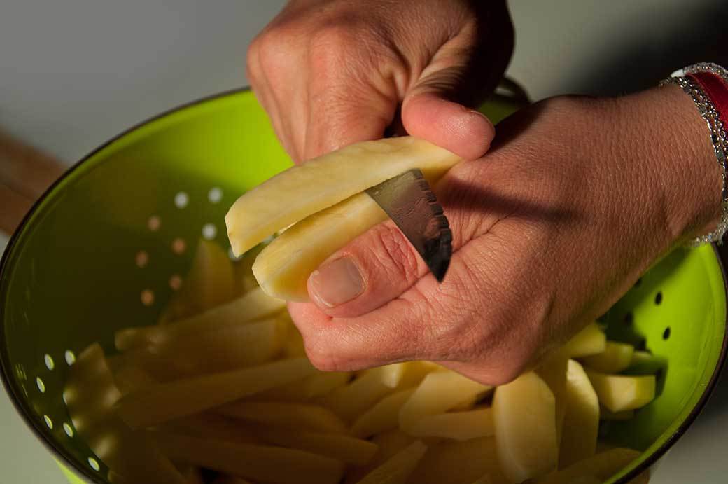 A pair of hands slice potatoes over a colander.