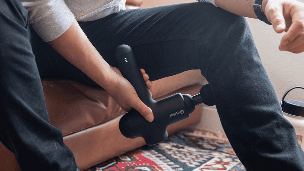 A young man is using the percussion massage gun on his left leg